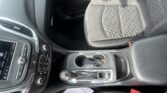Interior of a modern car showing the center console with gear shift, cup holders, and a touchscreen display on the dashboard; passenger seat visible to the right.