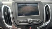 Infotainment screen showing the car's rearview camera with orange parking guide lines over a parking lot surface.