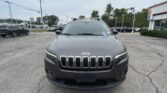 Front view of a gray Jeep SUV with a roof rack in a dealership parking lot at a wide-angle shot.