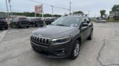 Gray Jeep SUV in the foreground at a car dealership lot, with other vehicles and signs in the background.