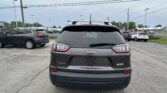 Rear view of a gray Jeep SUV with a roof rack in a parking lot, other cars and power lines in the background.