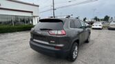 Gray Jeep SUV with roof rack parked in a car dealership lot beside a white building with large windows.