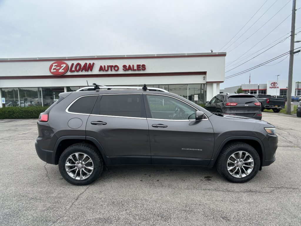 Gray Jeep Cherokee SUV in the foreground outside E-Z Loan Auto Sales; red E-Z LOAN sign on a white building.
