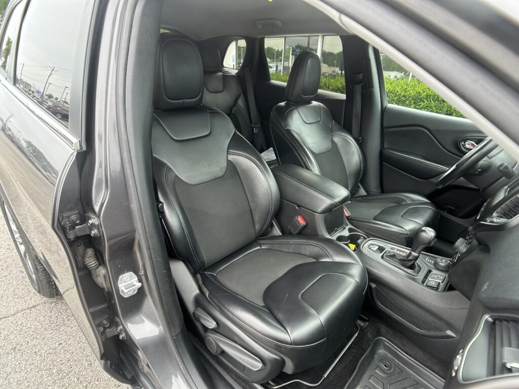Front interior of a dark leather SUV with two captain seats and center console, driver side door open