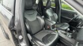 Front interior of a dark leather SUV with two captain seats and center console, driver side door open