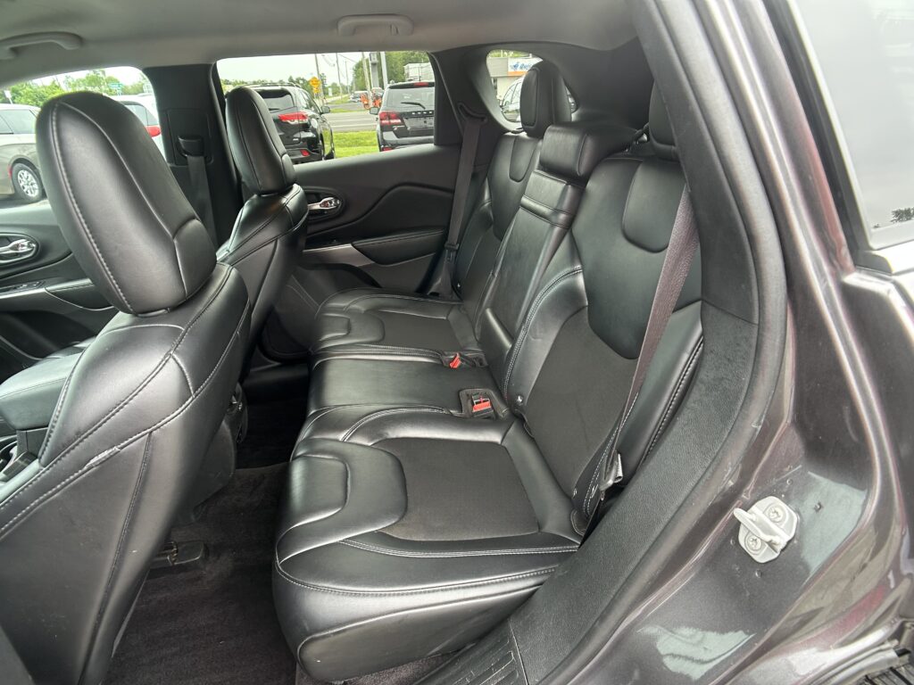 Rear interior of a car with black leather seats, three headrests, and visible seat belts.