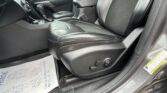 Front interior of a car showing black leather driver and passenger seats, center console with gear shifter, and a paper floor mat on the floor by the door edge.