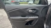 Interior car door panel with window controls, viewed from the front passenger seat. Outside: a parking lot with cars and a white sedan visible in the mirror.