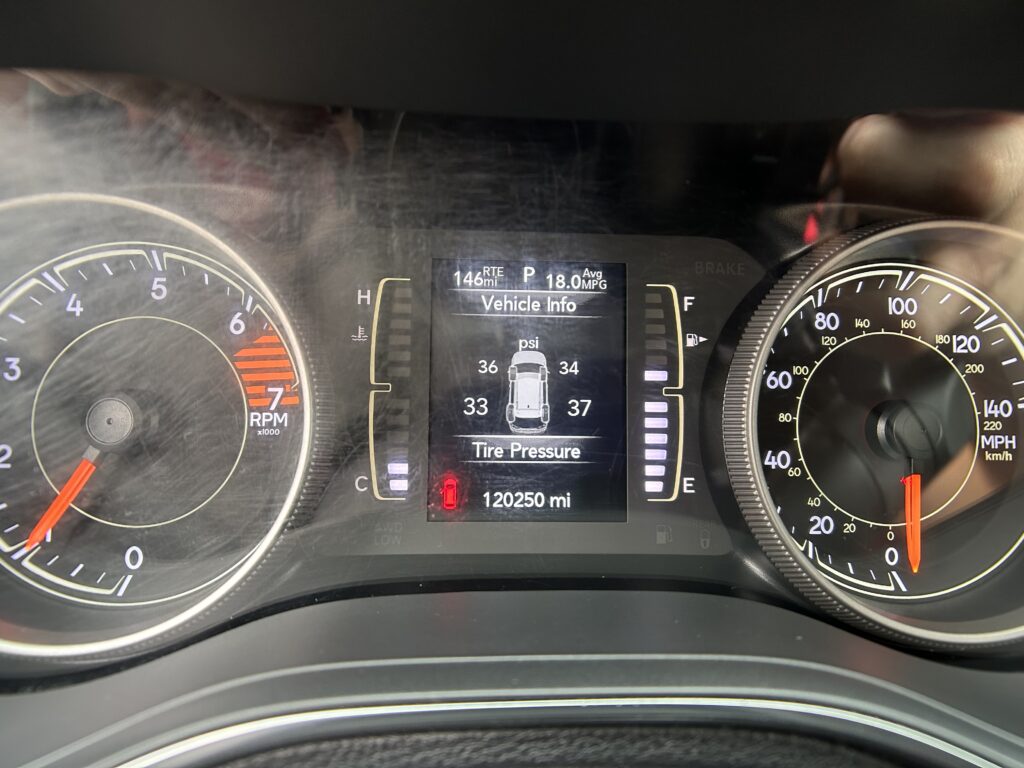 Close-up of a car instrument cluster: left tachometer, right speedometer, and a central digital display showing Vehicle Info, tire pressure, and odometer (120250 mi).