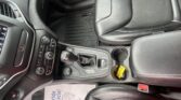 Center console of a car showing gear shifter, cup holder with yellow label, and leather seats nearby