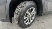 Close-up of a wet car tire and silver alloy wheel on a gray vehicle, showing rain droplets on the fender and pavement nearby.