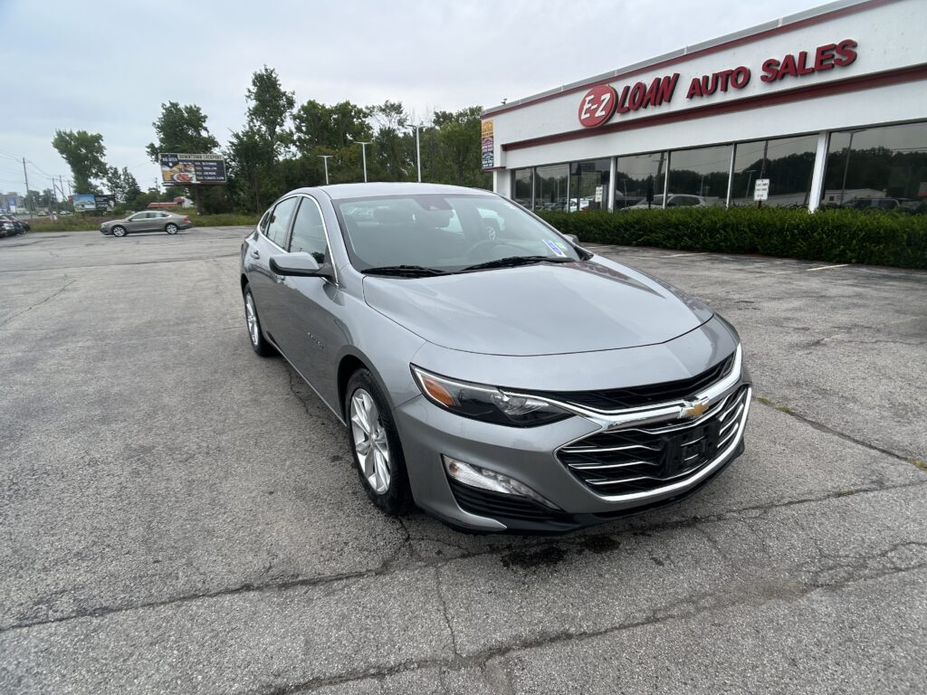 Front-left view of a silver Chevrolet sedan parked in a lot in front of EZ LOAN AUTO SALES storefront.
