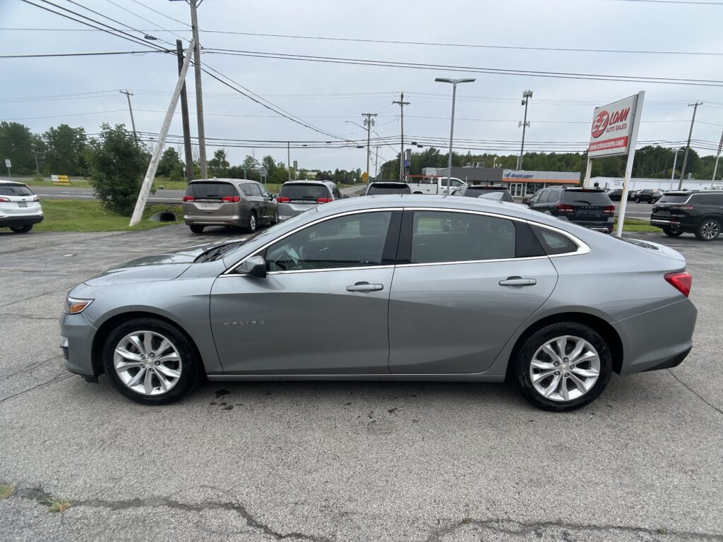 Silver Chevrolet Malibu foreground in a parking lot; utility poles and wires with an EZ Loan Auto Sales sign in the distance on the right.