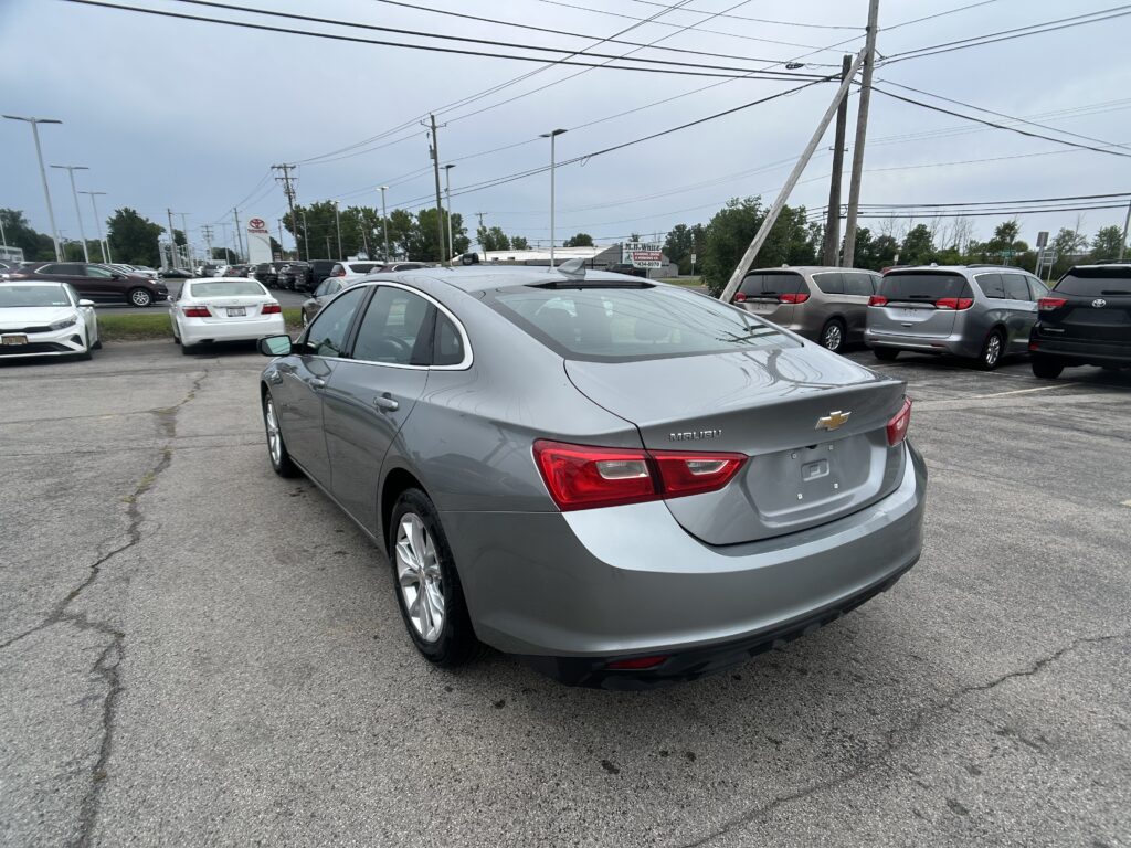 Rear view of a gray Chevrolet Malibu in a crowded car dealership lot with power lines overhead