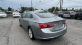 Rear view of a gray Chevrolet Malibu in a crowded car dealership lot with power lines overhead