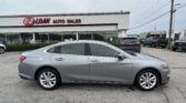 Silver Chevrolet Malibu parked in a car lot in front of EZ Loan Auto Sales storefront with glass windows and a red logo sign on the building.
