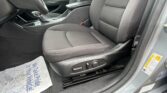 View of a car's front interior from the driver's side: dark fabric seats, center console with gear shifter, and seat adjustment controls; a protective paper mat lies on the floor near the front passenger seat.
