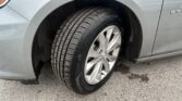 Close-up of a car's front wheel with a wet treaded tire and silver alloy rim, fender above.