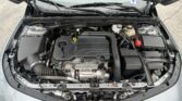 Engine bay of a car with ECOTEC cover, battery on the right, and various hoses and reservoirs visible under the hood.