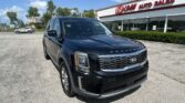 Black Kia Telluride in the foreground outside EZ Loan Auto Sales showroom on a sunny day with blue sky and other cars in the lot