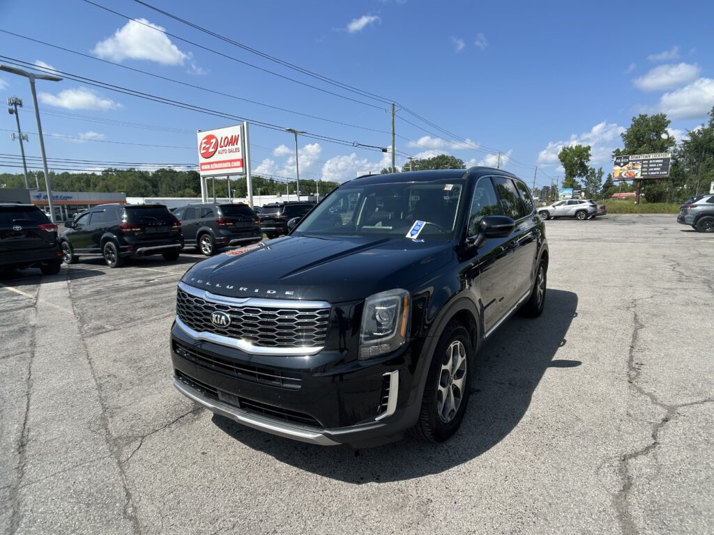 Front-left view of a black Kia Telluride SUV in a car dealership lot, with other SUVs and a large E-Z LOAN Auto Sales sign in the background and a clear blue sky above.