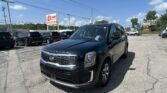 Front-left view of a black Kia Telluride SUV in a car dealership lot, with other SUVs and a large E-Z LOAN Auto Sales sign in the background and a clear blue sky above.