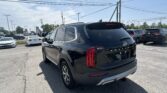 Rear three-quarter view of a black Kia Telluride SUV in a crowded car dealership lot, power lines overhead.