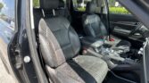 Black leather front seats in a car with a center console and sunlit interior visible through the open door
