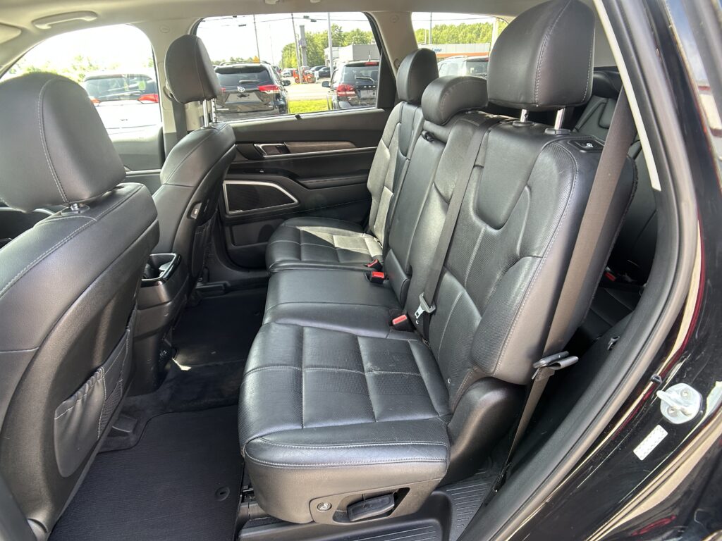 Rear interior of a black leather SUV with three seats, headrests, and visible seat belts in sunlight through the window a