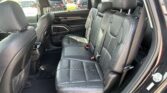 Rear interior of a black leather SUV with three seats, headrests, and visible seat belts in sunlight through the window a
