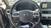 Driver's view of a Kia interior featuring a large steering wheel, instrument cluster, and a wide dashboard display screen in sunlight outside the windshield.