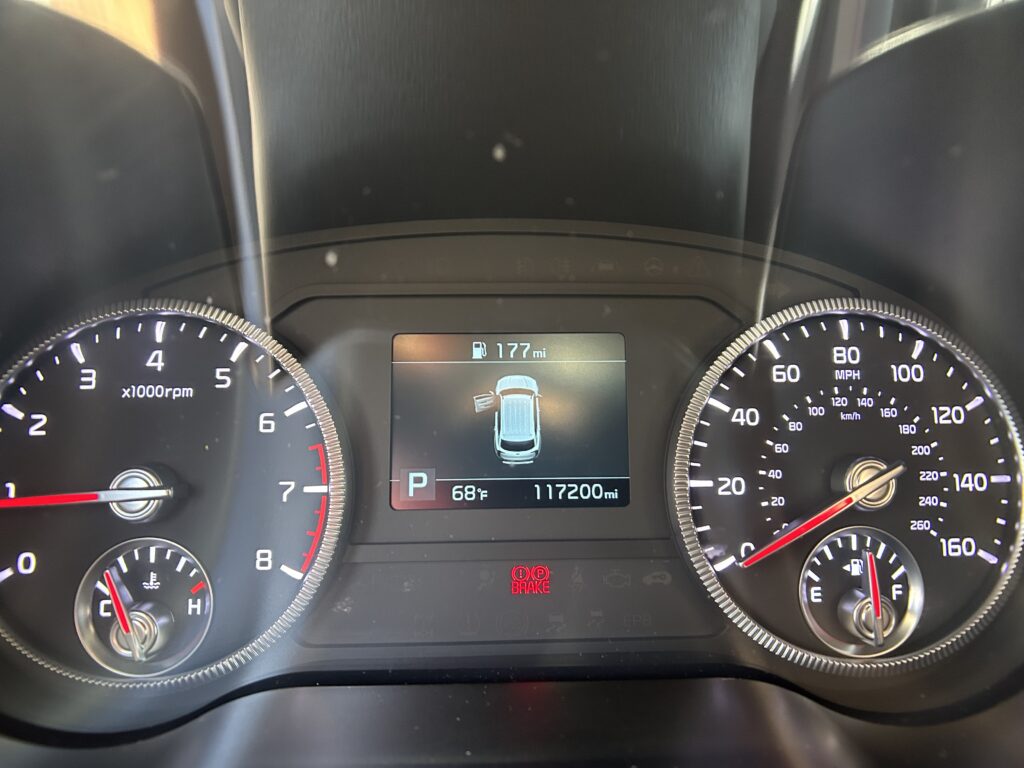 Car dashboard with speedometer and tachometer, center display shows fuel range 177 mi, odometer 11,7200 miles, gear in Park, temp 68°F.