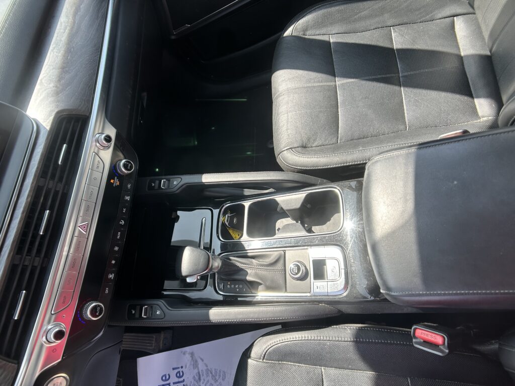 Interior of a car focusing on the center console: gear shifter, climate controls, and black leather seats with sunlight shadows