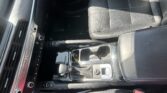 Interior of a car focusing on the center console: gear shifter, climate controls, and black leather seats with sunlight shadows