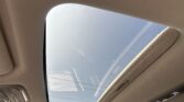 Beige car interior ceiling with a panoramic sunroof letting in blue sky.