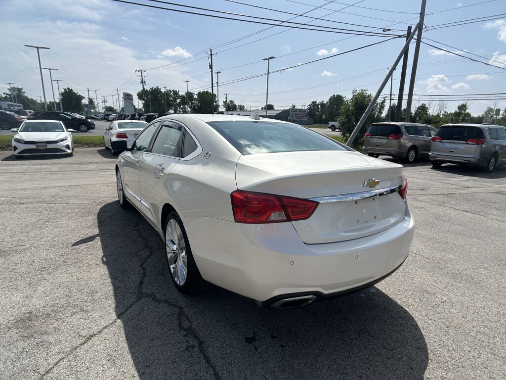 White Chevrolet sedan closest to the camera in a car dealership lot, with several other cars parked and power lines overhead.