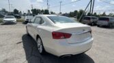White Chevrolet sedan closest to the camera in a car dealership lot, with several other cars parked and power lines overhead.