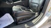 Front interior of a car with black leather seats, center console, gear shifter, and a seat belt buckle; paper on the floor near the door.