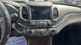 View of a car's dashboard from the driver's seat, showing a central touchscreen clock and climate controls; outside, a dealership parking lot with several cars.