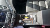 Front interior of a car showing black leather seat, center console with gear shifter and cup holder, sun glare on surface.
